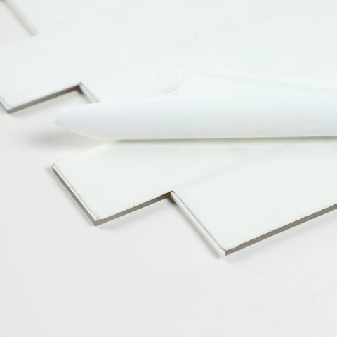 Close-up of glass peel and stick subway tile backsplash for kitchen, showing self-adhesive layer and no grout, 15"×12" size.