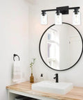 Three Light Vanity Bath Light Over Mirror In Deep Black With Clear Glass Cylinder Shades above bathroom sink