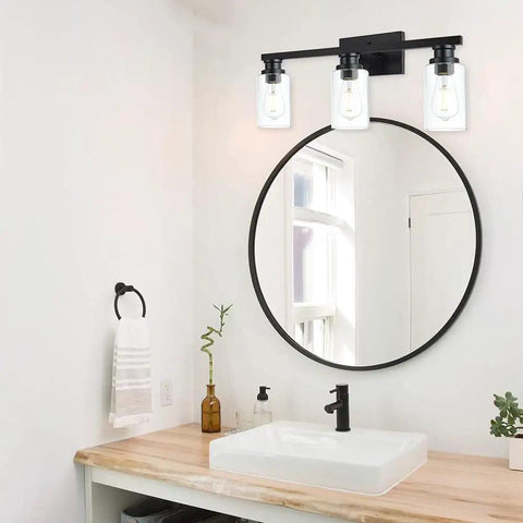 Three Light Vanity Bath Light Over Mirror In Deep Black With Clear Glass Cylinder Shades above bathroom sink