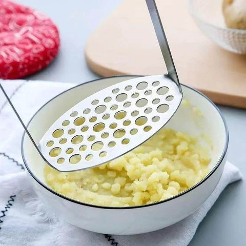Potato masher with perforated stainless steel disk above mashed potatoes in a white bowl.