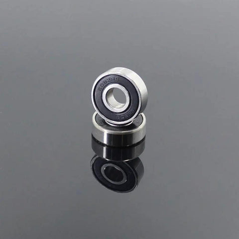 Pro Grade 608 2RS Hybrid Ceramic Bearings With Abec 7 Precision An 8 Pack Sized At 8X22X7MM For Skateboards And Roller Skates view of two ceramic bearings on a reflective surface.