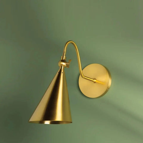 Lupe Wall Sconce Brass With Perforated Shade And Bowtie Swivel mounted against green wall