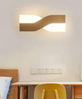UPRENXIAO Modern Minimalist Nordic Led Wall Sconce Wavy Twisted Design Baked mounted above a desk in a cozy bedroom setting.