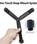 Hand holding Pocket Sized 2 In 1 Mini Tripod Desk Stand And Handheld Grip with one-touch snap mount system, black legs shown.