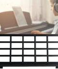 Black Keyboard Music Score Stand For Electronic Sheet Music in front of a child playing piano with headphones, focus on stand