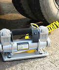 Kick Serious Fluid With This Straight Up Heavy Duty Electric Submersible Pump Built To Run Smooth On 12V Or 24V Power While Functioning As A Whisper Quiet Auto Air Compressor And Grit Proof Sump Pump on a surface near a tire.