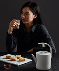 Sleek 850Ml Electric Brewing Kettle With Quick Boil Tech and Smart Auto Pour placed near snacks on a dark table.
