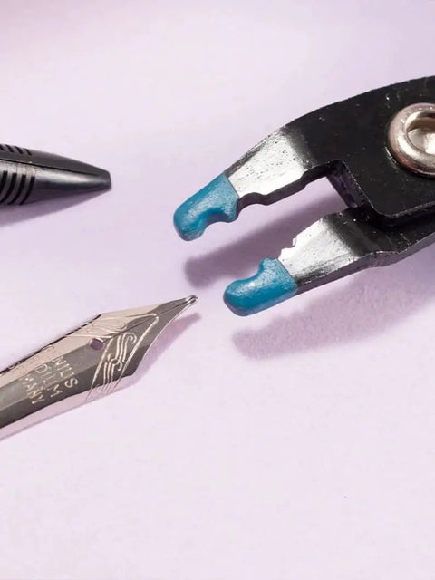 Close-up of a plier gripping a fountain pen nib with a Nib Removal Tool Kit With Plier And Rubber Sheet For Fountain Pen Nib Slit Widening And Protection.