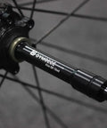 Close-up of Front 15mm Thru Axle to 9mm Quick Release Skewer Adapter on wheel hub, aluminum alloy, anodized black finish.