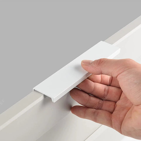 Hand holding one Six Pack Finger Edge Drawer Pull Handles In Bright White For Cabinets And Kitchen Drawers Hidden Mount Aluminum Hardware.