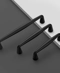 Three matte black cabinet handles, displaying sizes in a staggered row, showing a side view of the handle curvature and base.