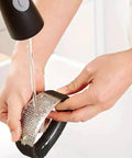 Person washing stainless steel garlic press rocker mincer with peeler under faucet, showcasing easy cleanup and rust resistance