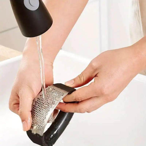 Person washing stainless steel garlic press rocker mincer with peeler under faucet, showcasing easy cleanup and rust resistance