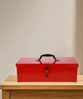 Slick Red Metal Toolbox Chest With Reinforced Carry Handle For Portable Gear Storage And Heavy Duty Tool Organization on a wooden surface.