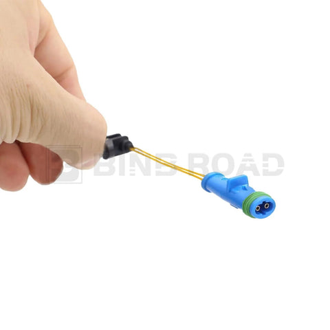 Close-up of blue brake pad wear sensor connector with yellow wires held in hand