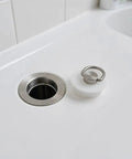 Silicone Drain Stopper for Kitchen Sinks and Bathtubs, White next to sink drain, featuring hanging ring for easy retrieval.