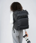 Person carrying Cube Camera Backpack For Filmmakers And Photographers Ultra Compact Dope Weatherproof Gear Bag with camera lens