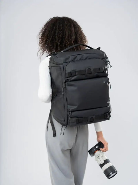 Person carrying Cube Camera Backpack For Filmmakers And Photographers Ultra Compact Dope Weatherproof Gear Bag with camera lens