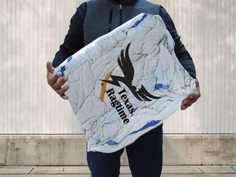 Person holding a large pack of Texas Ragtime rags wrapped in clear packaging, designed for cleaning purposes in various environments.