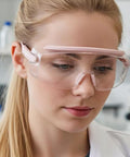 Safety goggles, front view, pink-framed with clear wraparound lenses worn over glasses.