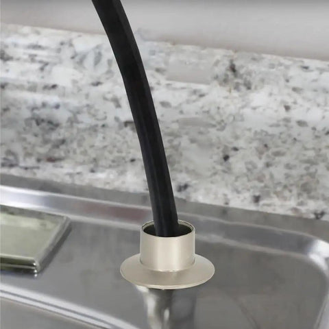 Heavy Duty Universal Faucet Hose Guide In Brushed Nickel with sprayer line coming out, mounted on kitchen sink deck.