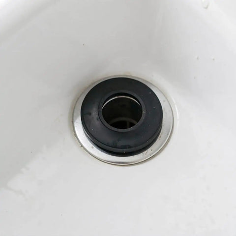 Close-up of a black rubber bathtub plug washer drain gasket replacement in a white sink.