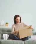 Woman on sofa opening box next to 50 Pack 16x16 Cushion Foam Pouches With Anti Static Film for moving and packing valuables