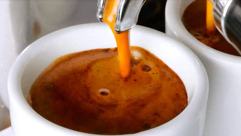 Close-up of espresso being extracted into a cup from a commercial espresso machine spout.