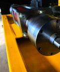 Close-up of waterjet intensifier pump assembly with metallic housing and drive shaft mounted on a yellow frame