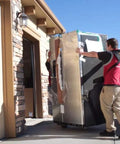 Shoulder Dolly 3500 two-person lifting system moves a large stainless steel refrigerator through a doorway.