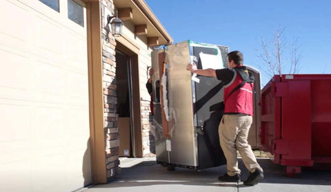 Shoulder Dolly 3500 two-person lifting system moves a large stainless steel refrigerator through a doorway.