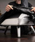 Person placing Karu 12 And Karu 2 Carry Cover Waterproof Weatherproof Shield on pizza oven, showing elastic lining and lightweight material.