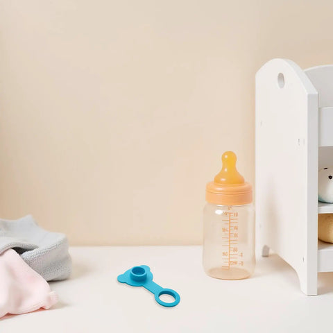 Blue Silicone Bathtub Drain Plug Stopper for Easy Removal on a clean table next to a baby bottle and soft cloths.