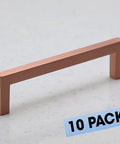 10 Pack Satin Copper Rose Gold Square Cabinet Hardware Euro Style Sleek Modern Bar Handle Pull 5 Inch Length 128 Mm Center To Center Includes 1 Inch And One And Five Eighths Inch Screws, shown on countertop, highlighting modern design.