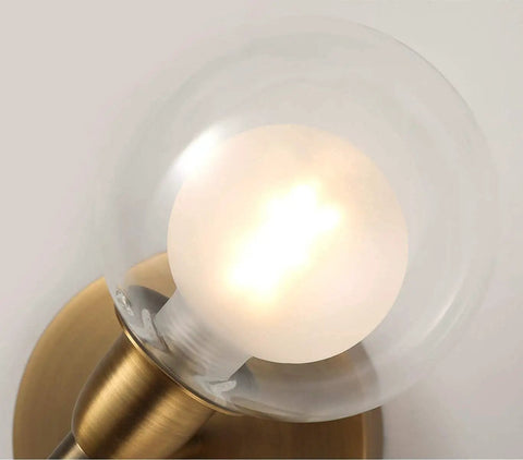 Rock This Mini Two Light Gold Bathroom Vanity Wall Sconce With Clear Glass Shades close-up of lit bulb in clear glass shade