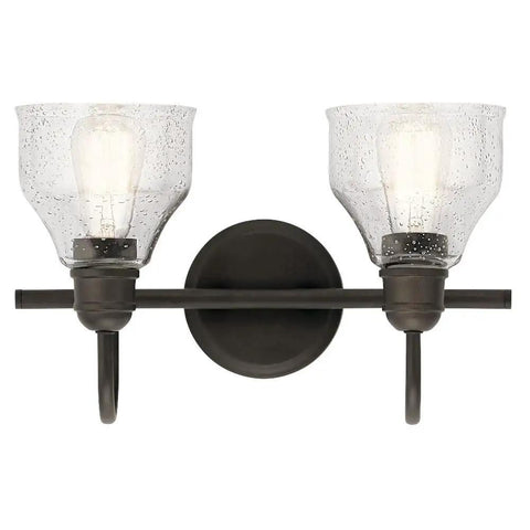 Avery 14.75 Inch Two-Light Vanity Light With Clear Seeded Glass In Olde Bronze, installed on a wall with lights on.