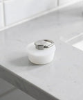 White Drain Stopper with Stainless Steel Ring, Silicone Seal Plug resting on a marble countertop by the sink.