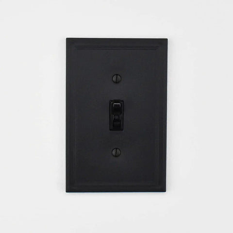 Black single toggle wall plate with a decorative cornice design on a white background.