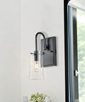 Three Light Vanity Light Fixture In Matte Black With Seeded Glass Shades For Bathroom mounted on white wall next to window