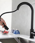Black Pull Out Deck Mounted Flexible Hot Cold Stream Shower Modes Nozzle Faucet in use, hand holding spray nozzle above sink.