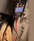 Close-up of Digital Clamp Meter With Autorange TRMS For Electricians measuring electrical panel, backlit display visible.