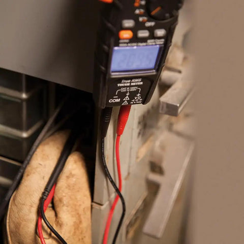 Close-up of Digital Clamp Meter With Autorange TRMS For Electricians measuring electrical panel, backlit display visible.