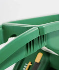 Close-up of a green handheld seed spreader with 6 lb capacity, easy grip handle, durable all-season design, for lawns and gardens.