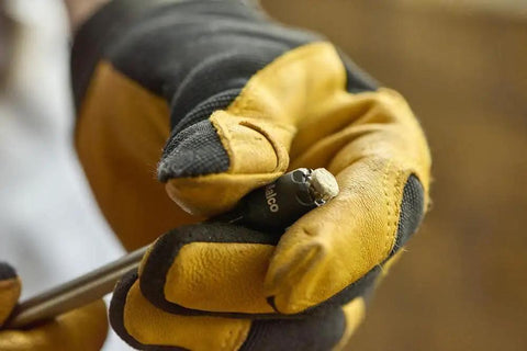 Gloved hand holding Reversible Hex Driver With 1/4 And 5/16 In Sockets, Sawtooth Sealant Cutter For Go To Fastener Removal, close-up view.