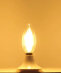 LED Filament E14 Candle Light Bulb 2700K Warm White, 400 Lumens glowing on a base, clear glass torpedo top, illuminated in warm light