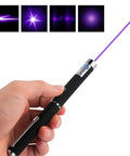 Hand holding a purple laser pointer for Three Pack Laser Pointer For Cats And Dogs Interactive Pet Toy Set With Red Green And Purple Lights Great For Playtime And Training Requires Two AAA Batteries Not Included.