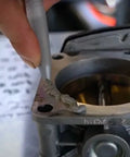 Permatex Ultra Grey RTV silicone gasket maker being applied to a metal carburetor gasket surface (close-up)
