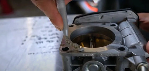 Permatex Ultra Grey RTV silicone gasket maker being applied to a metal carburetor gasket surface (close-up)