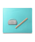 Turquoise silicone baking mat with stainless dough cutter and wooden rolling pin on a white background.