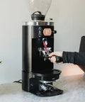 Pro Automatic Espresso Tamper in use with Mahlkonig E80 Grinder, showcasing durable matte black shell, precise tamping process.